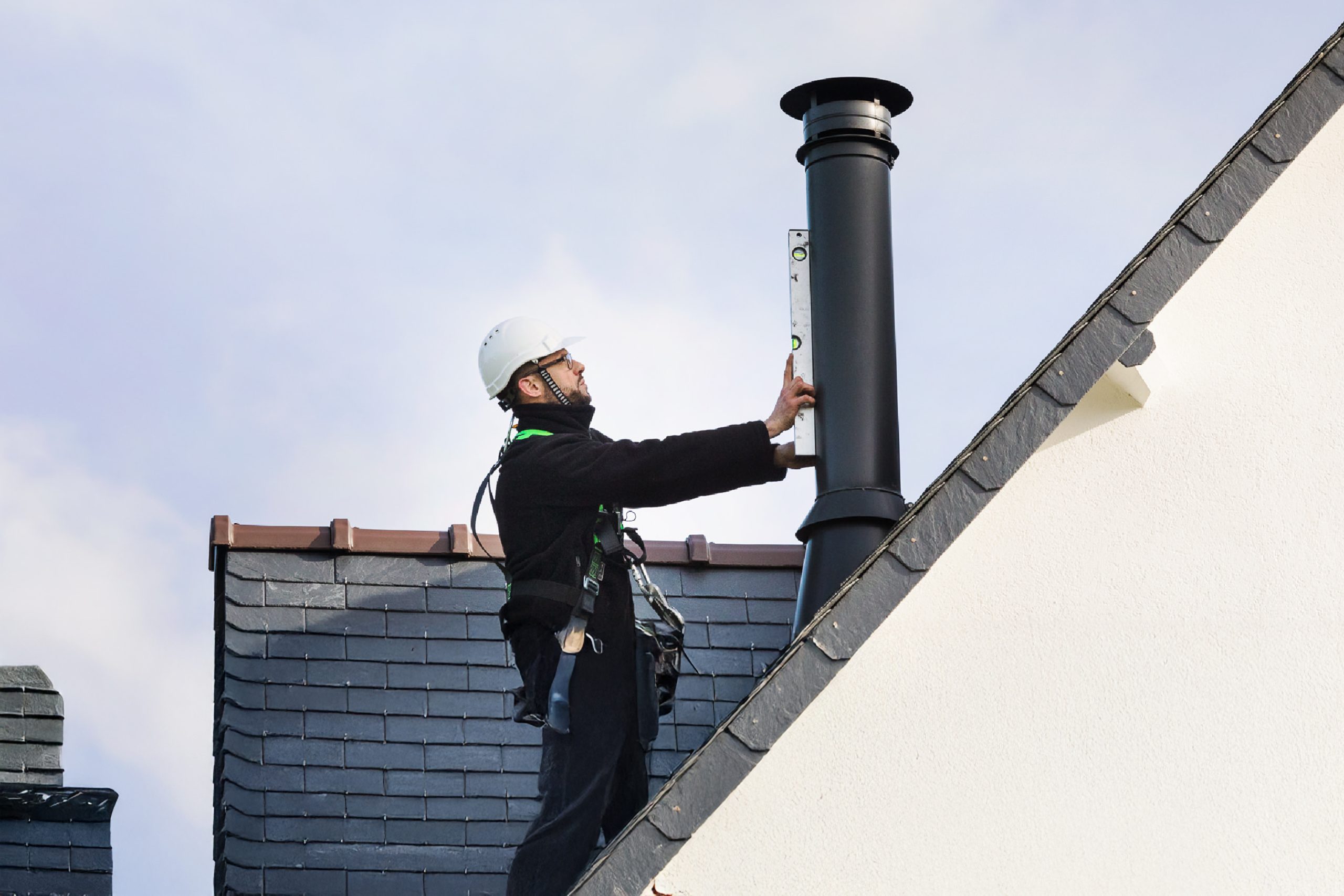 Technicien sur toiture vérifiant l’alignement d’un conduit de fumée avec un niveau à bulle